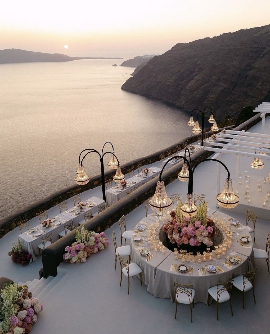 Une réception privée sur une terrasse surplombant la mer au coucher du soleil, avec des tables fleuries et des luminaires suspendus